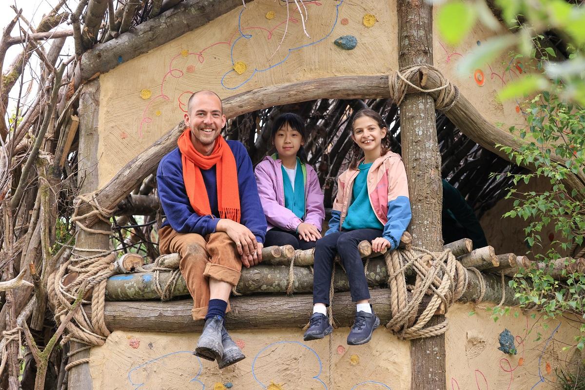 Harry Holding, garden designer, with children from Sulivan Primary School in the den at the The RHS No Adults Allowed Garden.