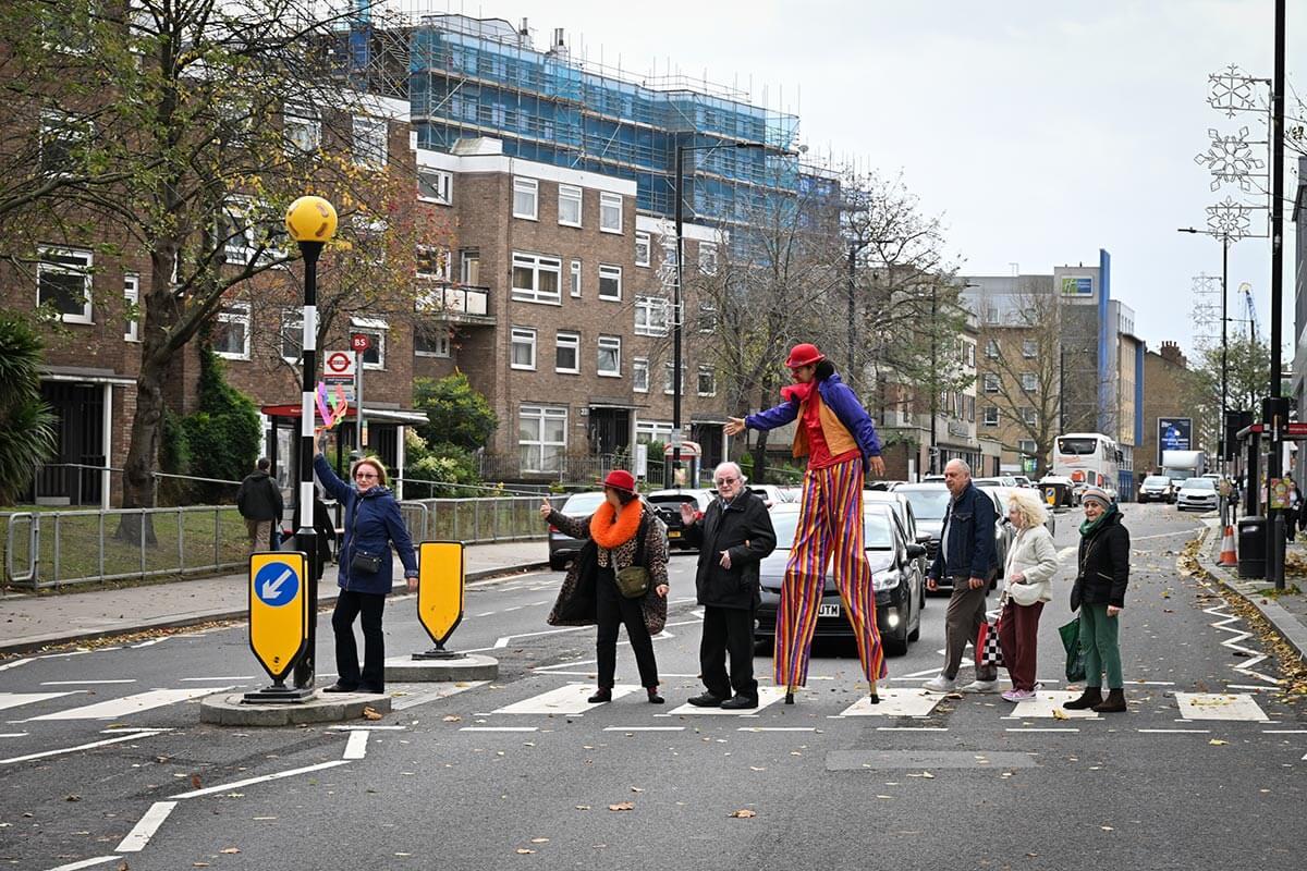 Maystar Residents’ Association committee members, including Debbie Golt (left) and Michael Gannon, MRA Co-Chair (middle) walking across the zebra crossing on North End Road with stilt-walker Ella the Great