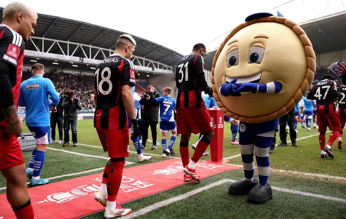 Crusty, the Wigan mascot, welcomes the Fulham squad to the Brick Community Stadium