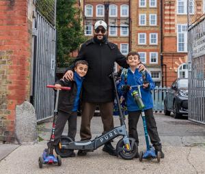 Father and sons on scooters outside the school gates.