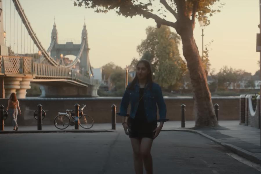 Emma (Ambika Mod) leaving her flat in One Day, with Hammersmith Bridge in the background.